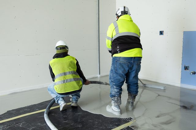 Hose discharging gypsum slurry over black acoustic mat